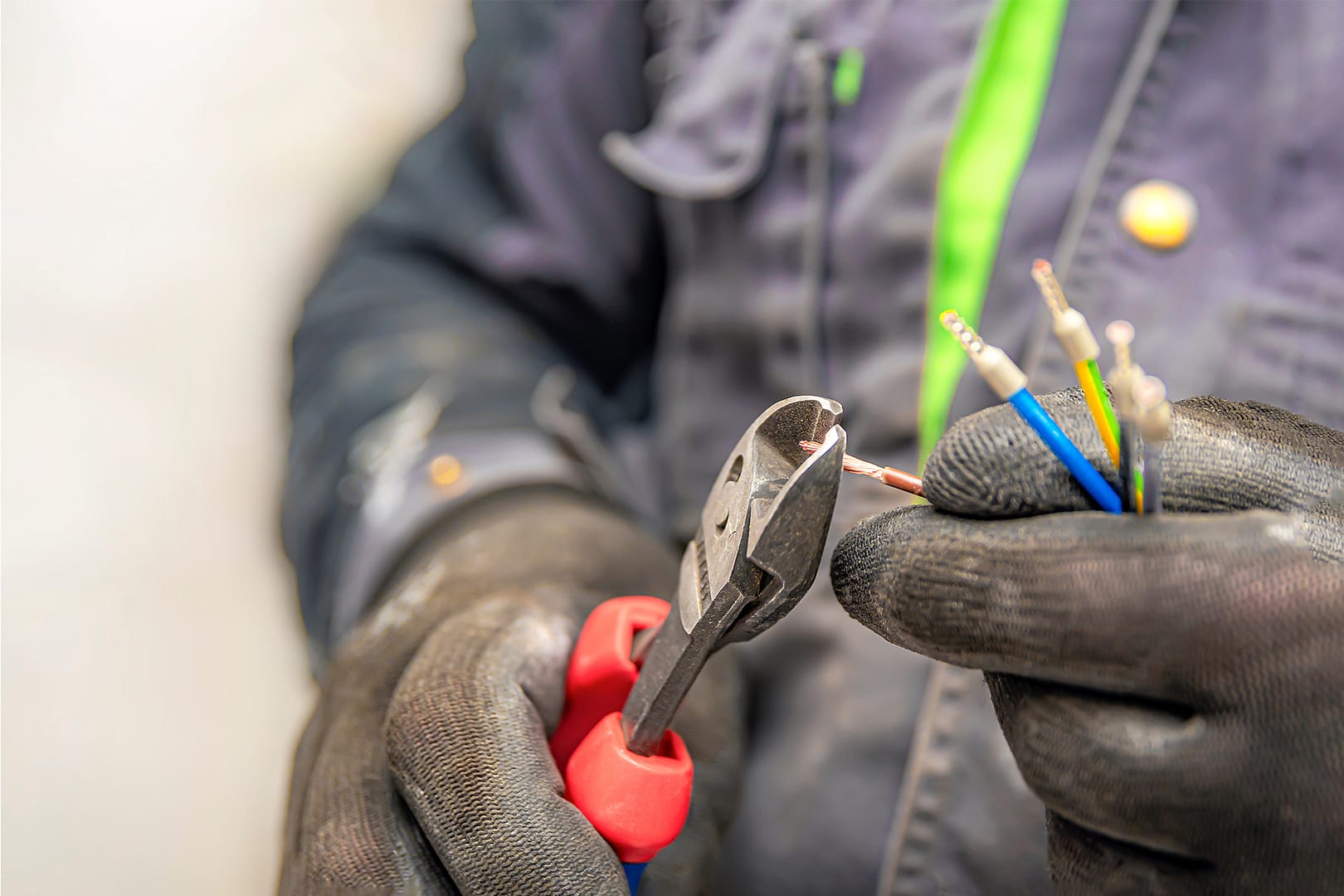 a close up of an electrician using pliers to strip the conductive sheath from the end of a wire in a three phase setup