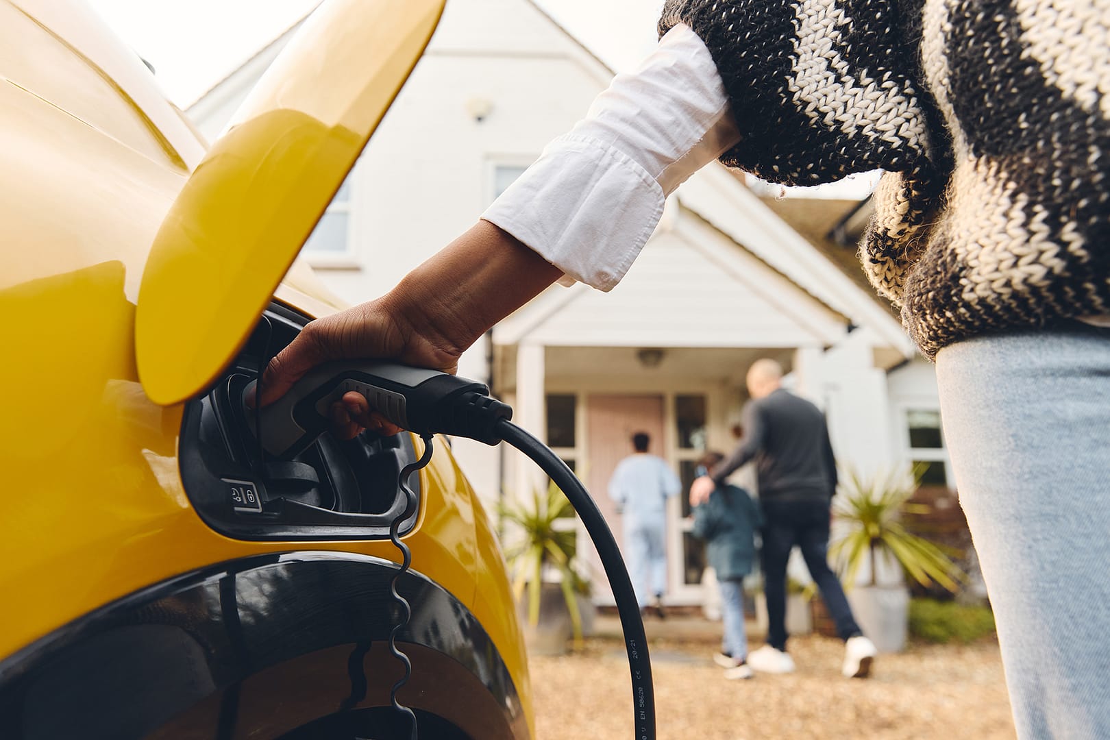 a mother plugging in an ev charger as the rest of the family make their way into the home
